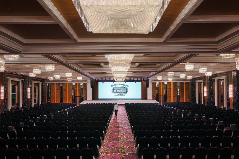 Conference hall at The Majestic set theatre style facing a stage and screen under crystal chandeliers